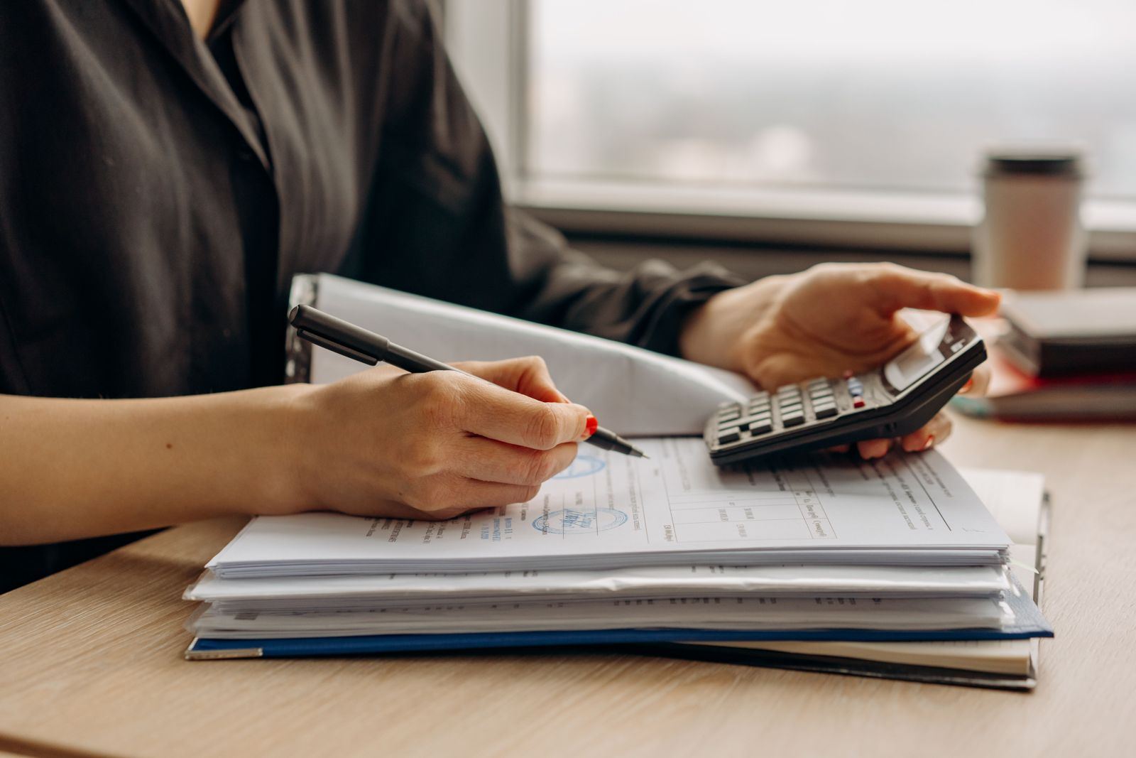 Accountant checking figures on a calculator beside a stack of paperwork